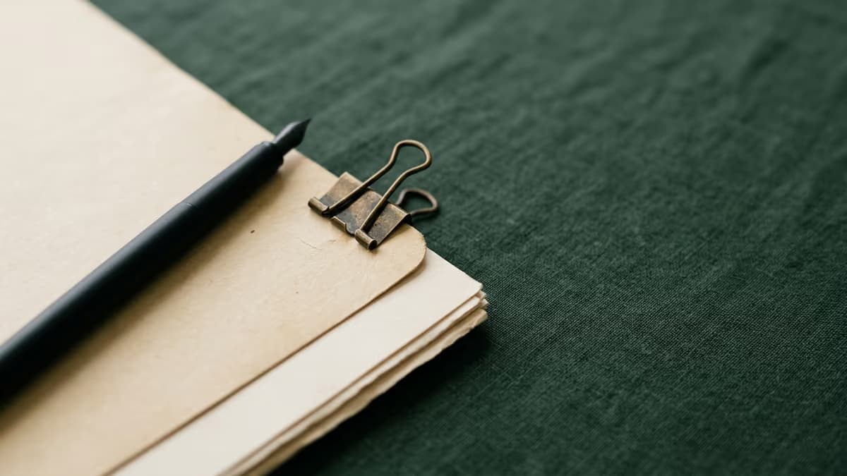 A clipped stack of plain documents and a pen on a calm green surface, representing organizing a business tax return