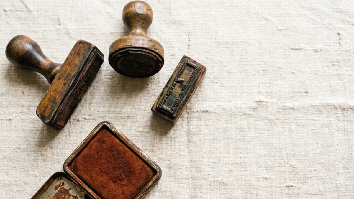 Three vintage rubber stamps arranged in a triangular layout on a raw linen surface with a small rust-colored ink pad, shot from overhead, warm earth tone palette