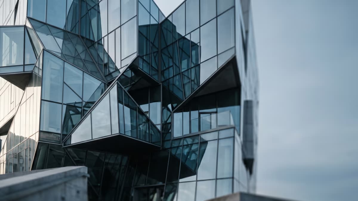 Abstract modern architectural facade with stacked glass boxes and geometric intersecting planes in a cool blue and steel gray palette, soft natural light, editorial blog hero composition