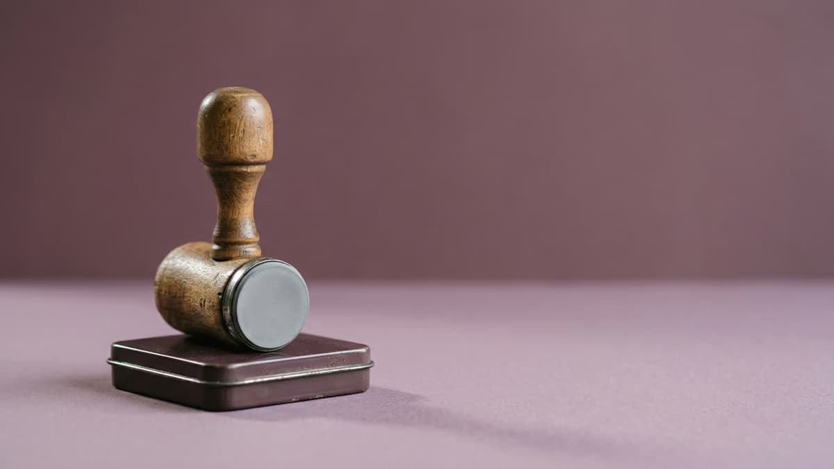 A single wooden-handled rubber stamp resting on an ink pad against a smooth muted plum background