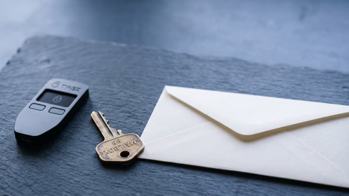 Macro still life of a small hardware crypto wallet, a brass mailbox key, and a sealed business envelope on a slate surface in cool indigo light, no people, editorial composition with negative space on the right