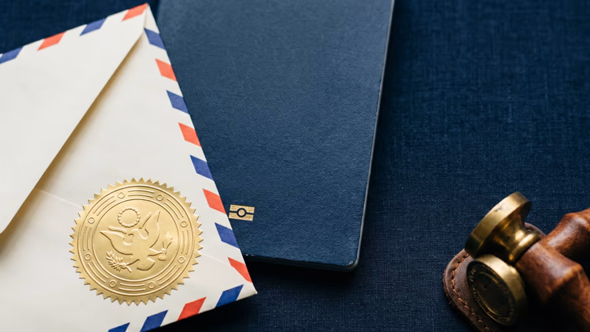 Embossed apostille seal pressed onto a folded international envelope beside a passport and a brass stamp on a navy linen desk under directional cool light, editorial overhead composition
