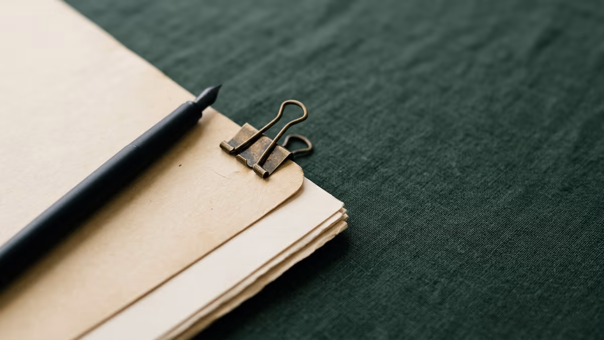 A clipped stack of plain documents and a pen on a calm green surface, representing organizing a business tax return