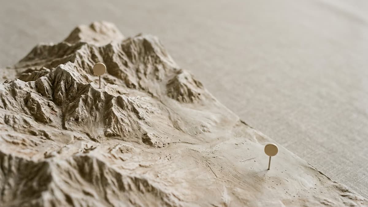 Two small pins standing on a softly lit relief model of mountains and plains, suggesting two different states