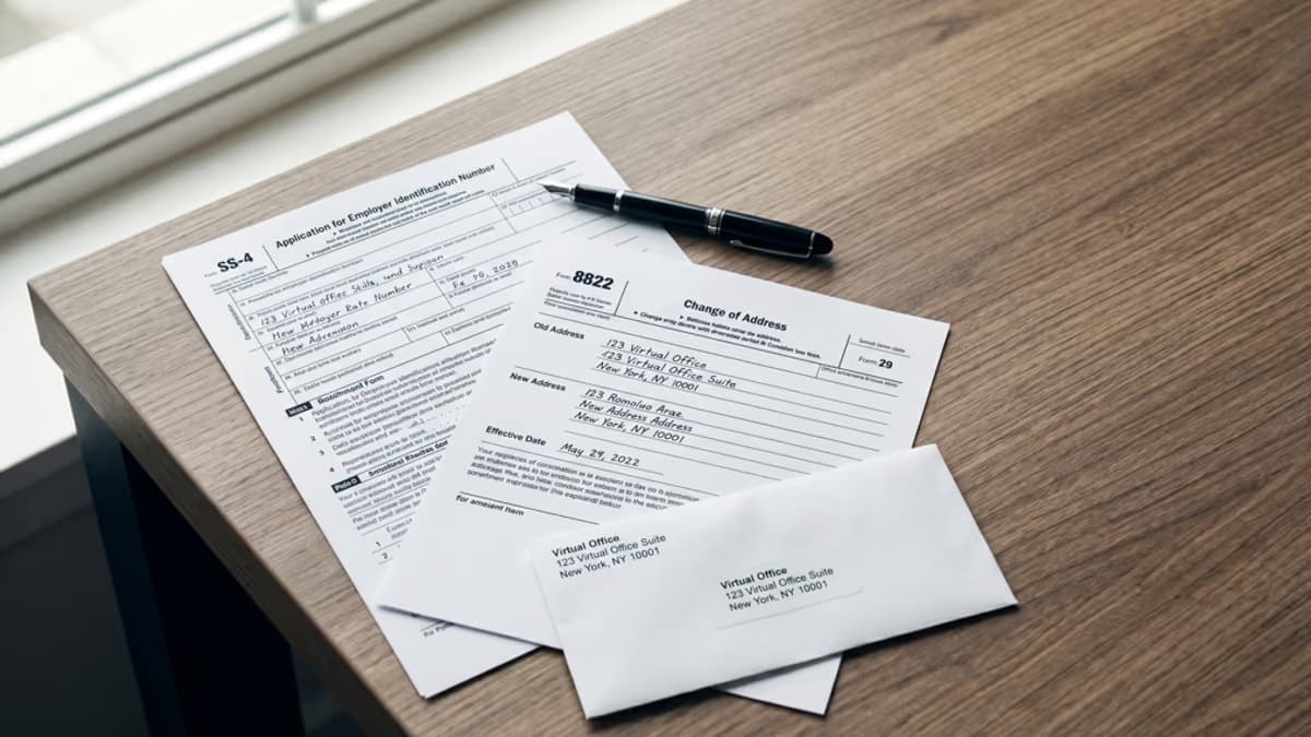 An IRS Form SS-4 next to a Form 8822 change of address form on a desk, with a virtual office address slip and a fountain pen