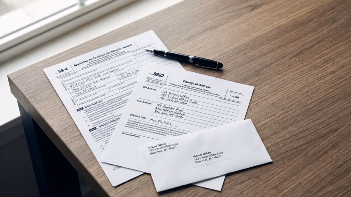 An IRS Form SS-4 next to a Form 8822 change of address form on a desk, with a virtual office address slip and a fountain pen