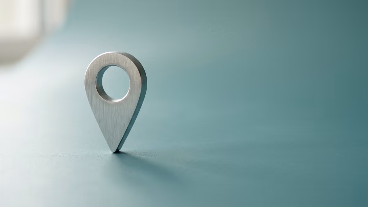 A single metallic location pin standing on a clean teal surface, representing one verifiable business address that a platform check can confirm
