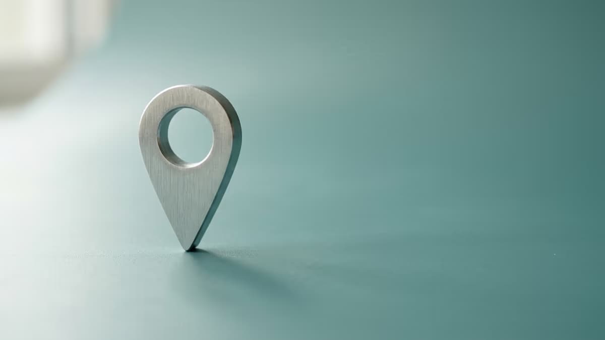 A single metallic location pin standing on a clean teal surface, representing one verifiable business address that a platform check can confirm