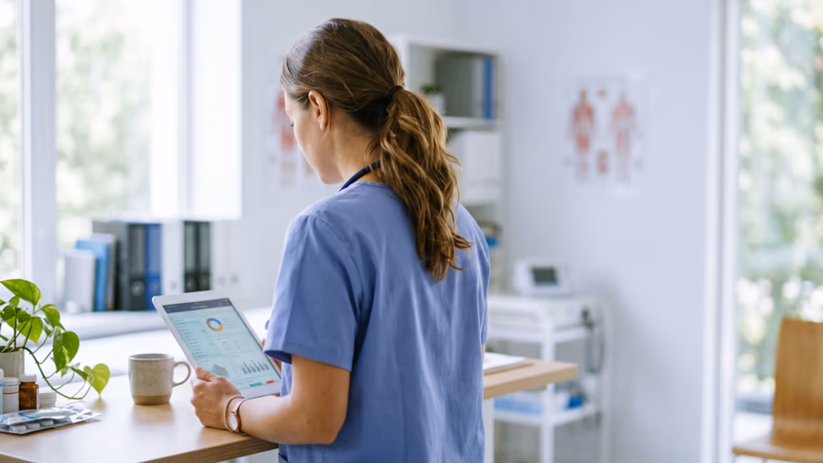 A home health care professional reviewing enrollment paperwork at a desk in a small clinical office, soft natural window light, muted indigo and cream palette