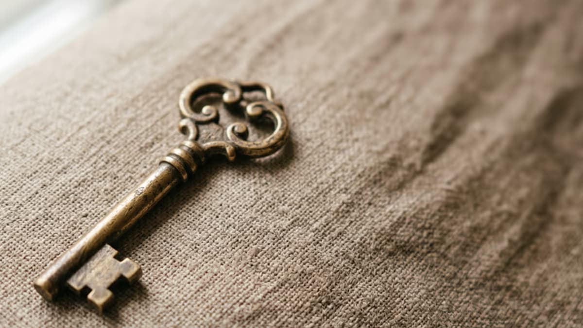 Antique brass key on a warm beige textured surface with soft natural window light captured from above in editorial macro composition