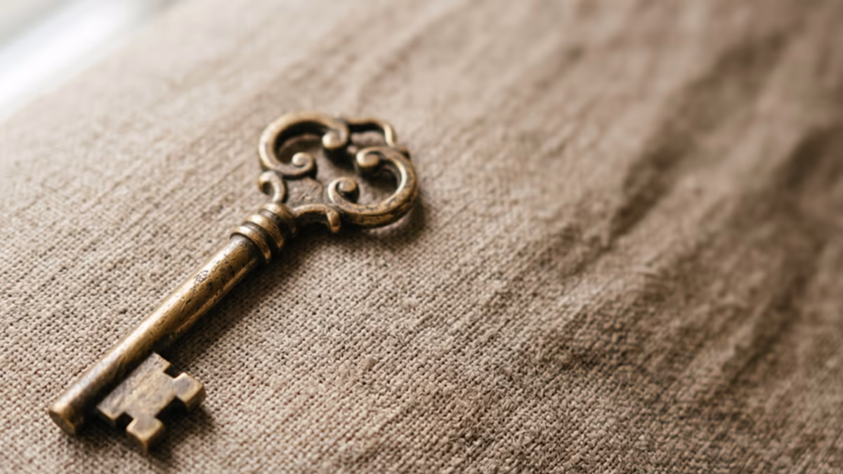 Antique brass key on a warm beige textured surface with soft natural window light captured from above in editorial macro composition
