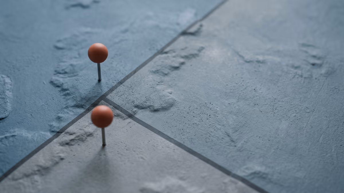 Two identical map pins standing on opposite sides of a state boundary line on a minimalist unlabeled map
