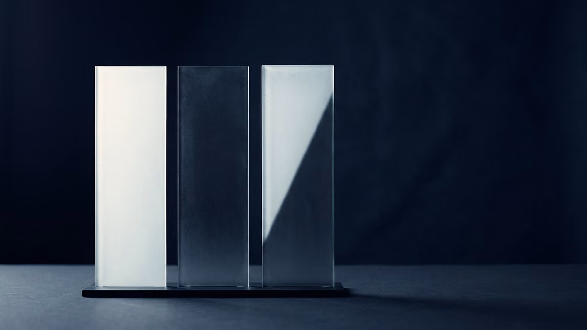 Three identical frosted glass panels standing in a row against a deep indigo backdrop, each lit from a different angle so one glows pale, one stays in shadow, and one is only half lit