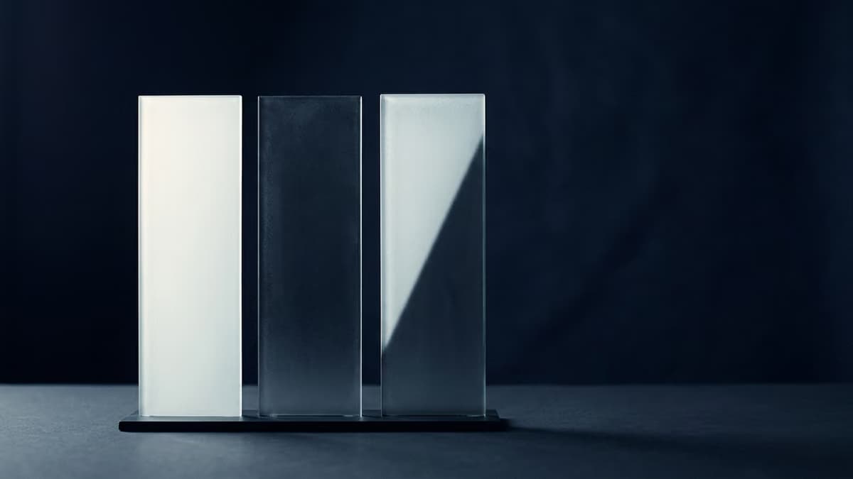 Three identical frosted glass panels standing in a row against a deep indigo backdrop, each lit from a different angle so one glows pale, one stays in shadow, and one is only half lit