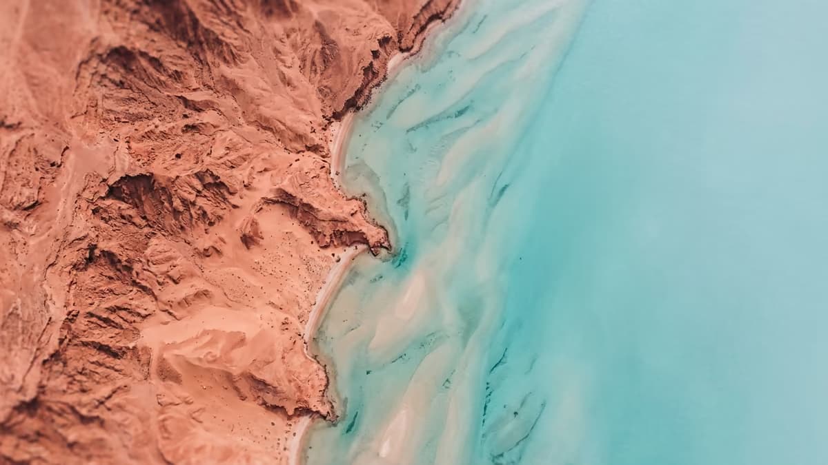 Aerial view where red desert rock fades into clear turquoise shallow coastal water