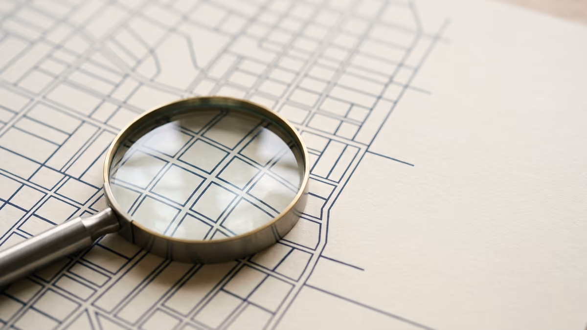 A magnifying glass resting on a softly blurred abstract street-grid pattern, representing verifying which documents prove a business address