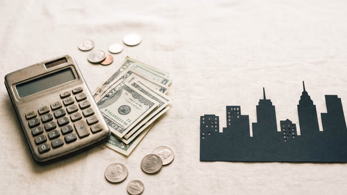 Calculator, US dollar bills, and a small city skyline silhouette on a wooden desk illustrating the hidden fees behind a virtual office price