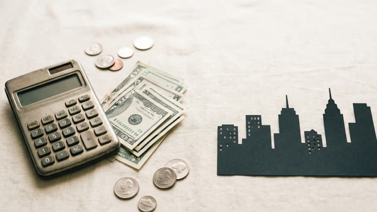 Calculator, US dollar bills, and a small city skyline silhouette on a wooden desk illustrating the hidden fees behind a virtual office price