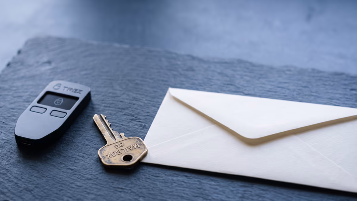 Macro still life of a small hardware crypto wallet, a brass mailbox key, and a sealed business envelope on a slate surface in cool indigo light, no people, editorial composition with negative space on the right